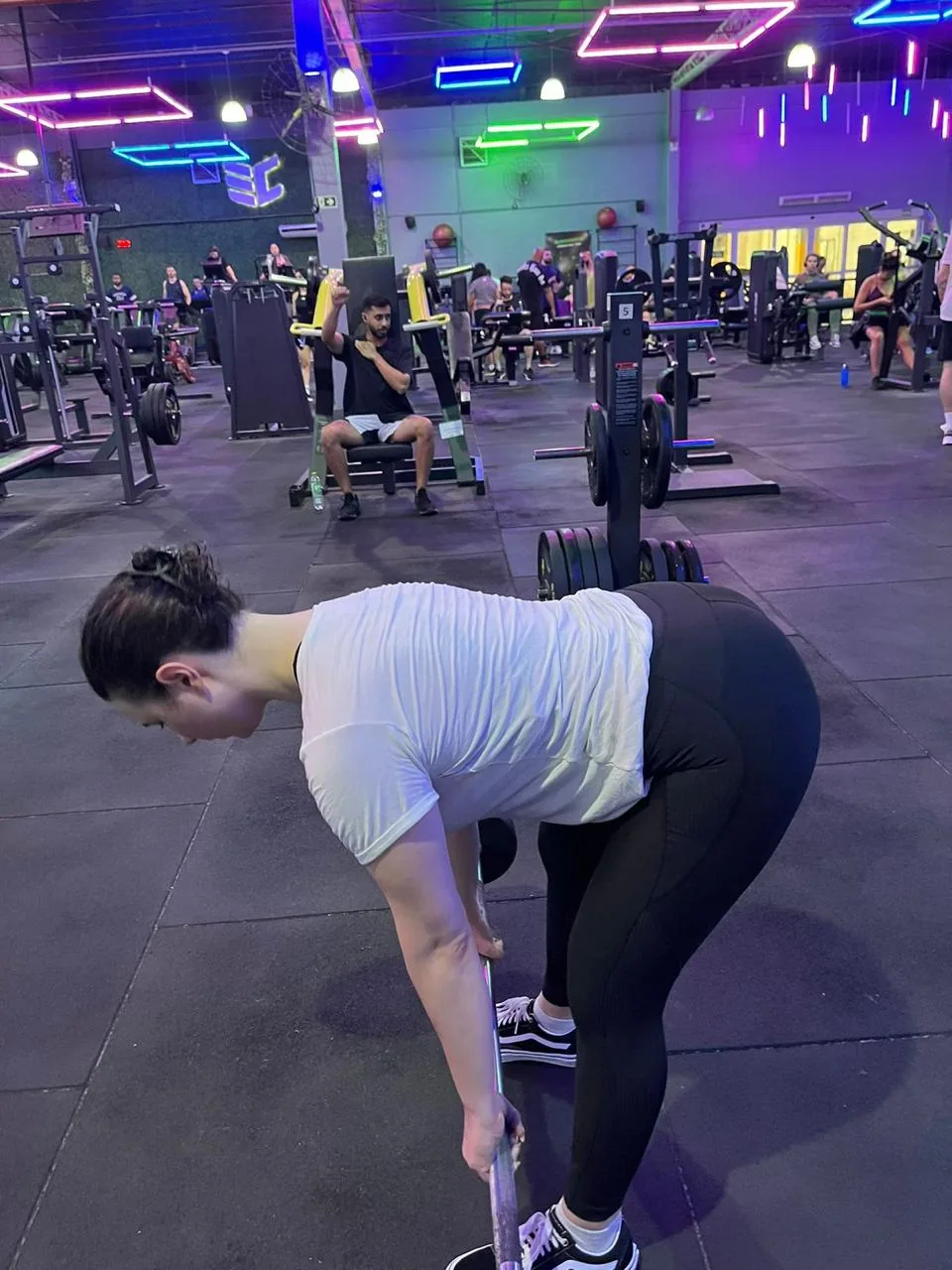 Aluna realizando exercício com barra na academia.